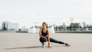 Young woman in black sportswear stretching outdoors in a sunny urban environment.