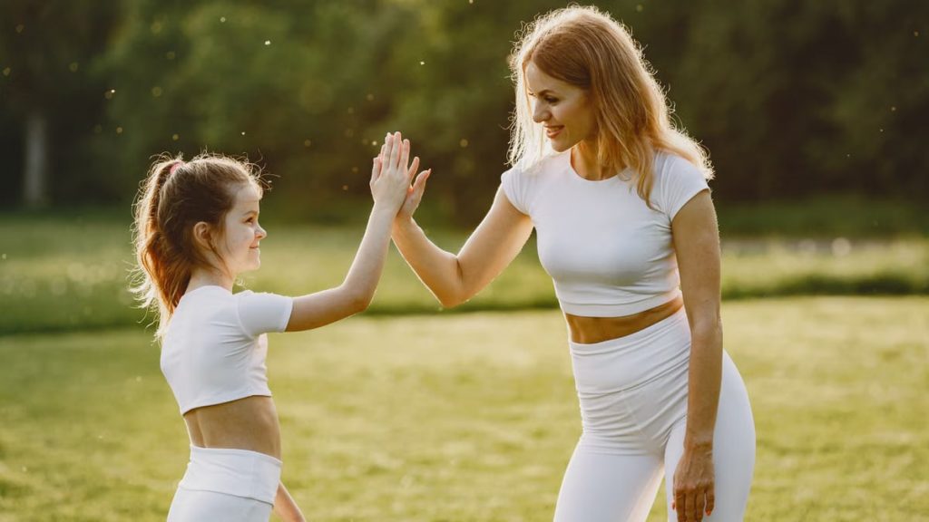 A mother and daughter high-fiving in matching outfits outdoors.