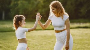 A mother and daughter high-fiving in matching outfits outdoors.